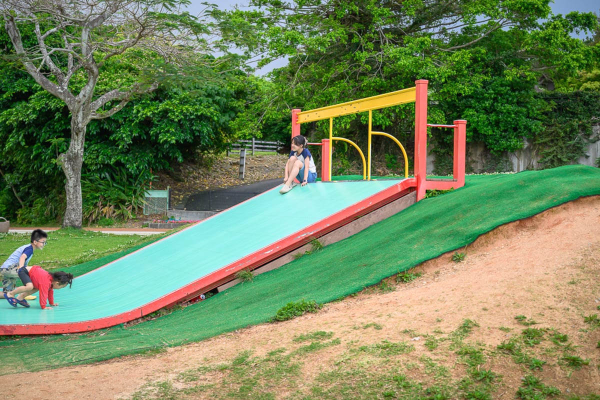 整理日本沖繩那霸沖繩縣營奧武山公園的親子遊樂設施，包含草坡溜滑梯、沙坑、龍形造型遊具與階梯區，並說明園內運動設施、適合停留的動線與帶小孩時的注意事項。