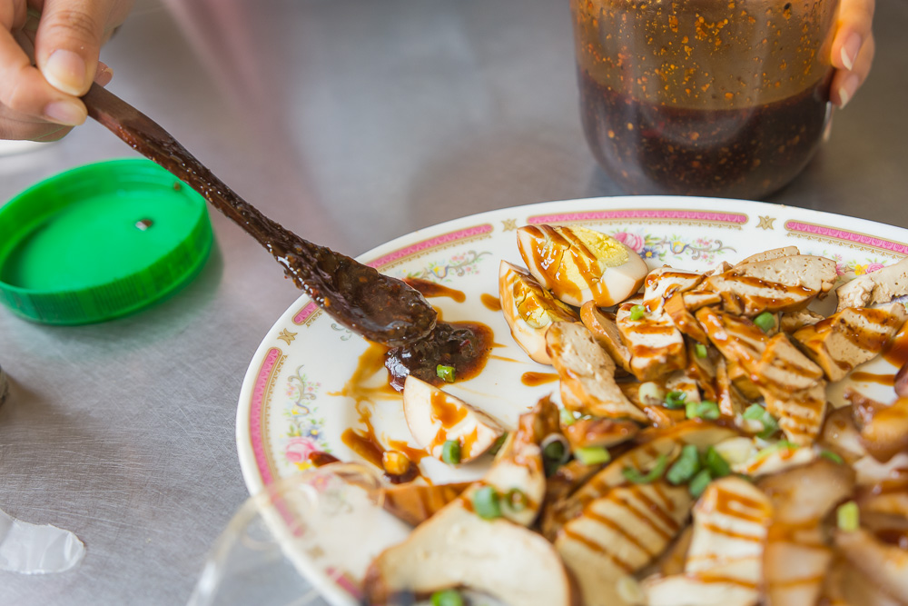 苗栗外省牛肉麵|牛肉麵配酸菜與辣椒油,滷豆干、豬耳朵切盤可當小菜 6 苗栗外省牛肉麵|手持湯匙淋醬汁於滷味拼盤,金屬桌面,旁有醬料罐。