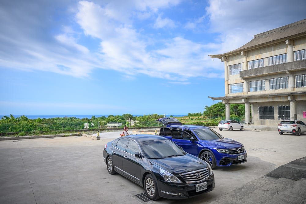 新北石門貝殼廟｜停車場，黑色轎車，藍色休旅車，中式建築，遠山，大海，藍天白雲
