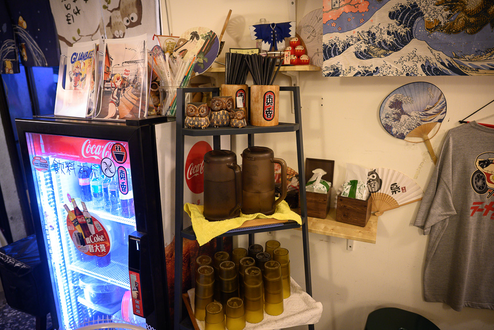 台中火曜二代目拉麵｜日式拉麵店內，展示架擺放水壺、杯具與貓頭鷹雕塑，旁有可口可樂冰箱與裝飾扇。