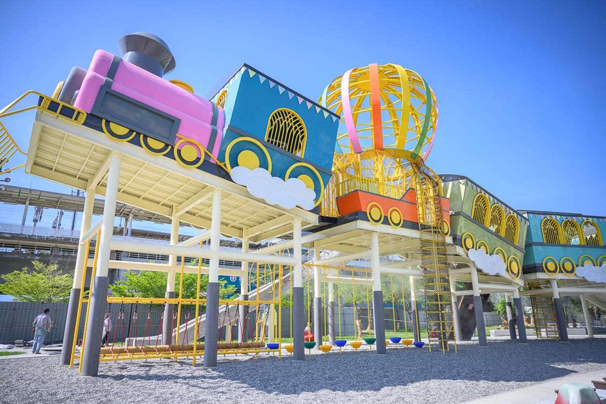 屏東林邊車站公園｜大型彩色火車造型遊具，高架鋼柱，攀爬網，溜滑梯，戶外公園，藍天，碎石地地面，遊樂場。