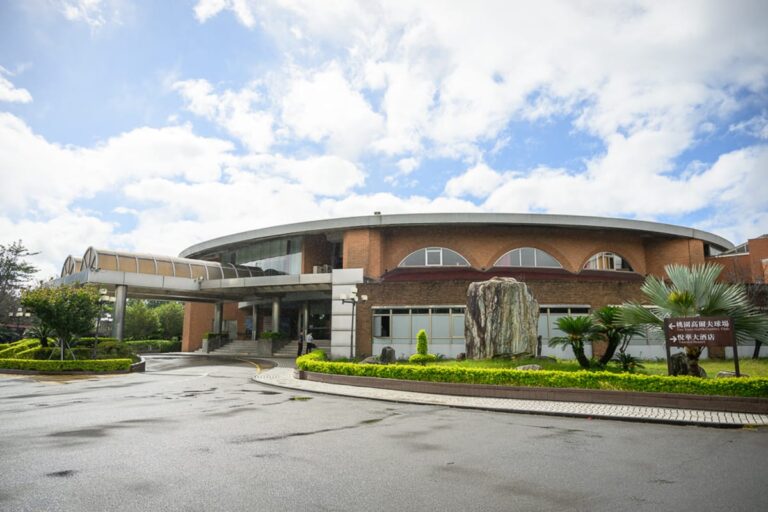 桃園悅華大飯店完整指南|露營車住宿與度假設施 18 桃園悅華大飯店|圓形紅磚建築、車道、景觀石、綠樹、藍天白雲。建築外觀呈圓弧狀,屋頂設有半圓形拱窗,前方有迴車彎與柏油