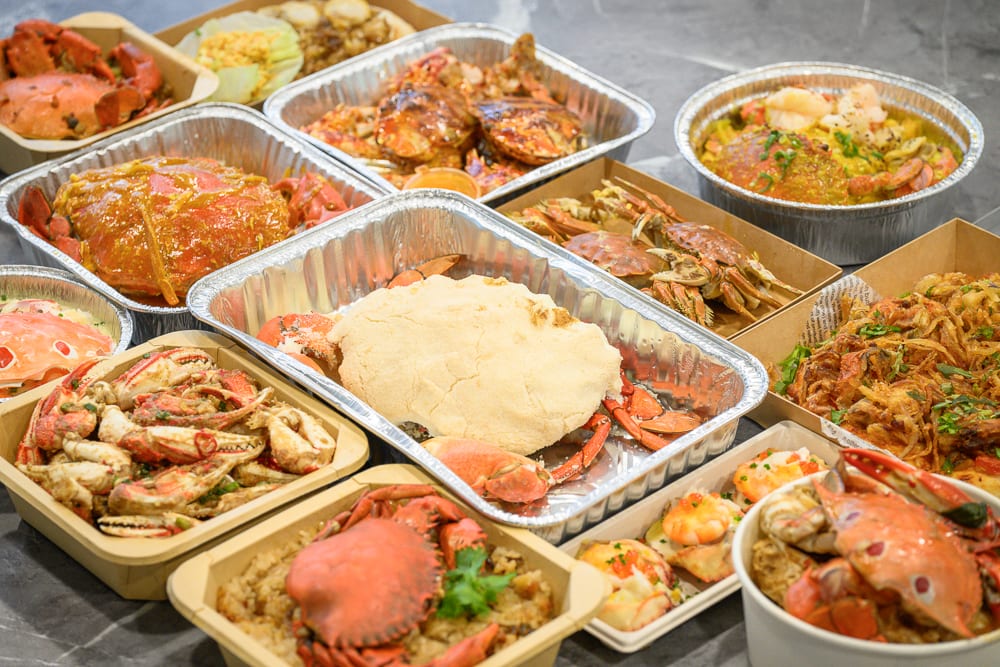 台中阿布潘水產｜料理，多個鋁箔盒與紙盒盛裝多樣蟹肉海鮮餐點，滿桌蟹黃、炒蟹與焗烤料理。
