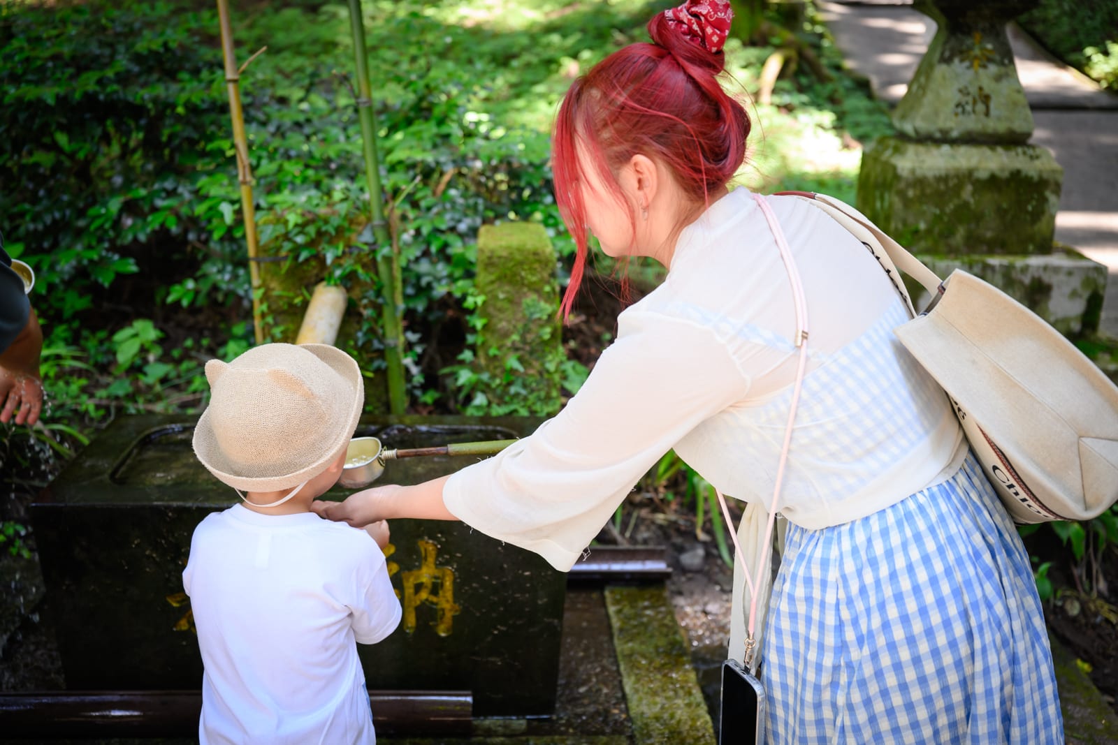 日本熊本-上色見熊野座神社｜紅髮綁包頭的女子與戴圓帽的孩童，石造水手舍，竹子，寺廟，樹林，白色上衣，藍白格紋長裙。
