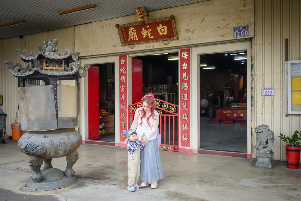 桃園白蛇廟｜寺廟、銅香爐、紅門、白蛇廟匾額，女子與孩童站在建築外水泥地，兩側對聯，石獅雕像，招牌，鐵皮牆面。