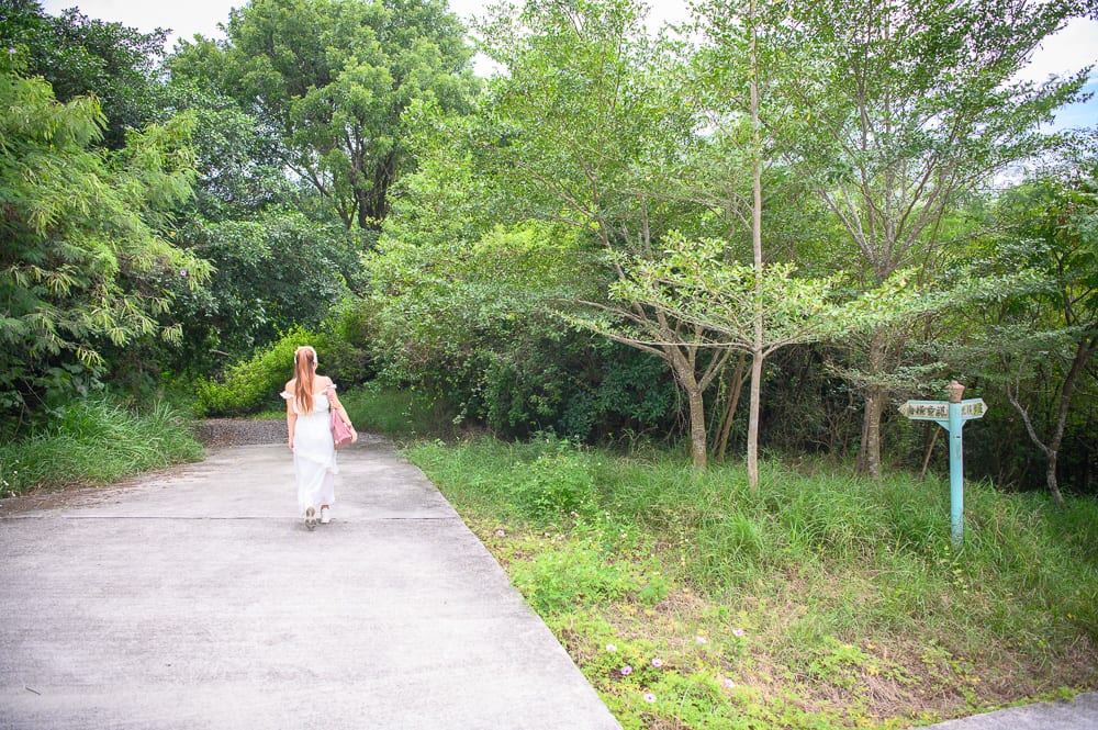 高雄漯底山步道｜長髮女子，白色長裙，水泥路，樹林，綠草地，藍色指標牌，戶外。