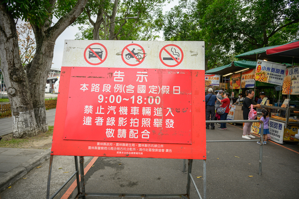 雲林古坑綠色隧道路口紅色告示牌，寫著本路段例假日9:00至18:00禁止汽機車輛進入，後方是小吃攤位