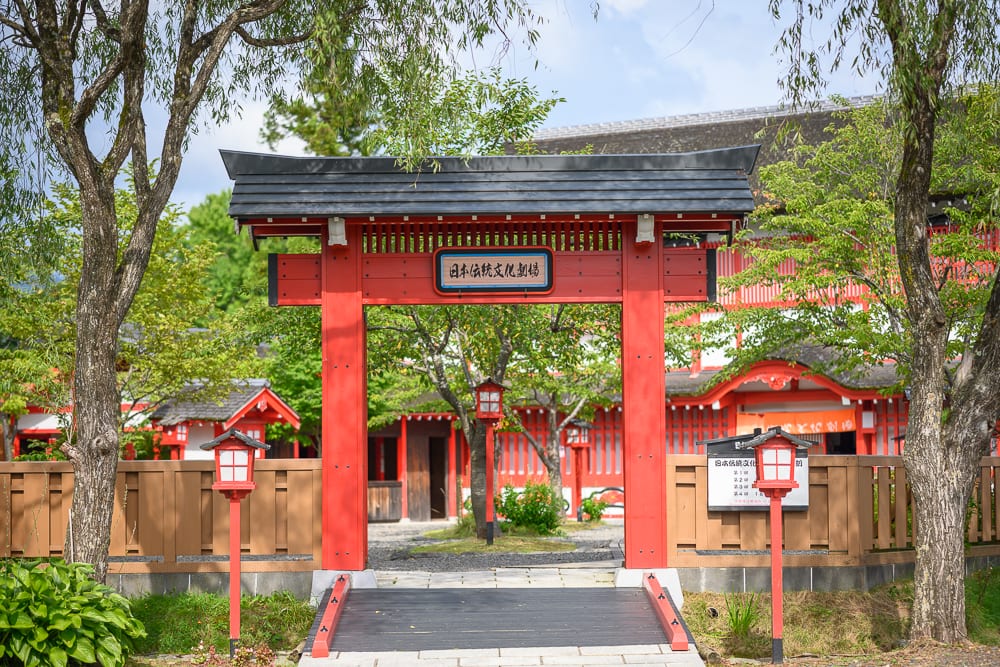 日本登別伊達時代村完整指南|江戶街景與庭園展示 3 日本登別-依達時代村|紅色木製牌樓、黑色斜瓦屋頂、木造圍籬、紅色燈籠、石板小徑、綠樹、傳統建築群、藍天白雲。
