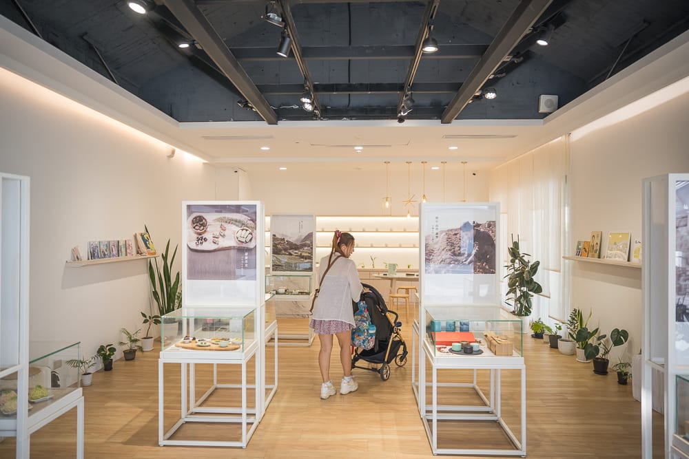 新北坪林茶業博物館完整指南|茶業歷史展覽與品茗體驗 12 新北坪林茶業博物館|室內,女性,嬰兒車,展示台,木地板,白色牆面,軌道燈具,盆栽植物,層架,展品。
