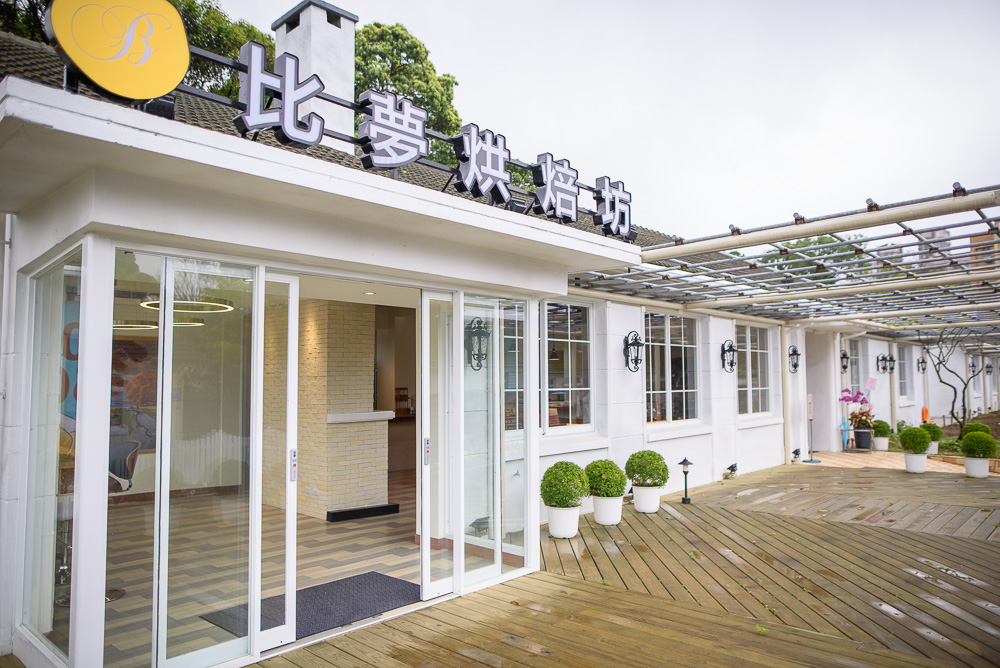台北比夢烘焙坊｜比夢烘焙坊，白色建築，玻璃門，木質露台，盆栽。